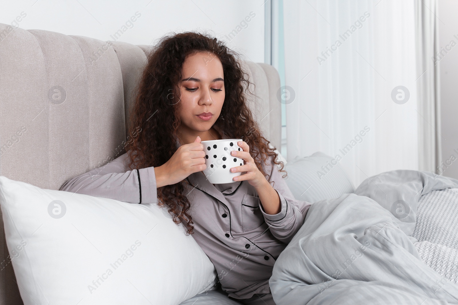 Photo of Beautiful African American woman with cup of drink in bed at home