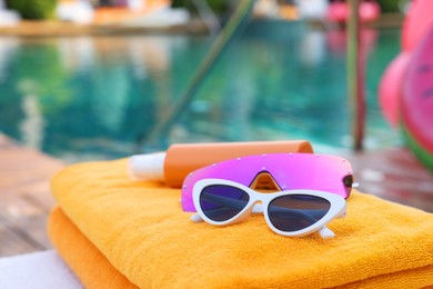 Beach towels, sunglasses and sunscreen on sunbed near outdoor swimming pool. Luxury resort