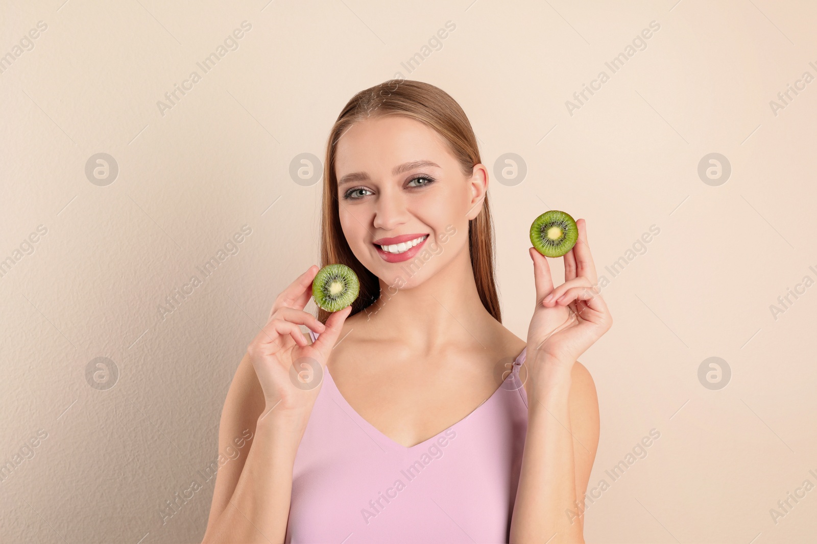 Photo of Young woman with cut kiwi on beige background. Vitamin rich food