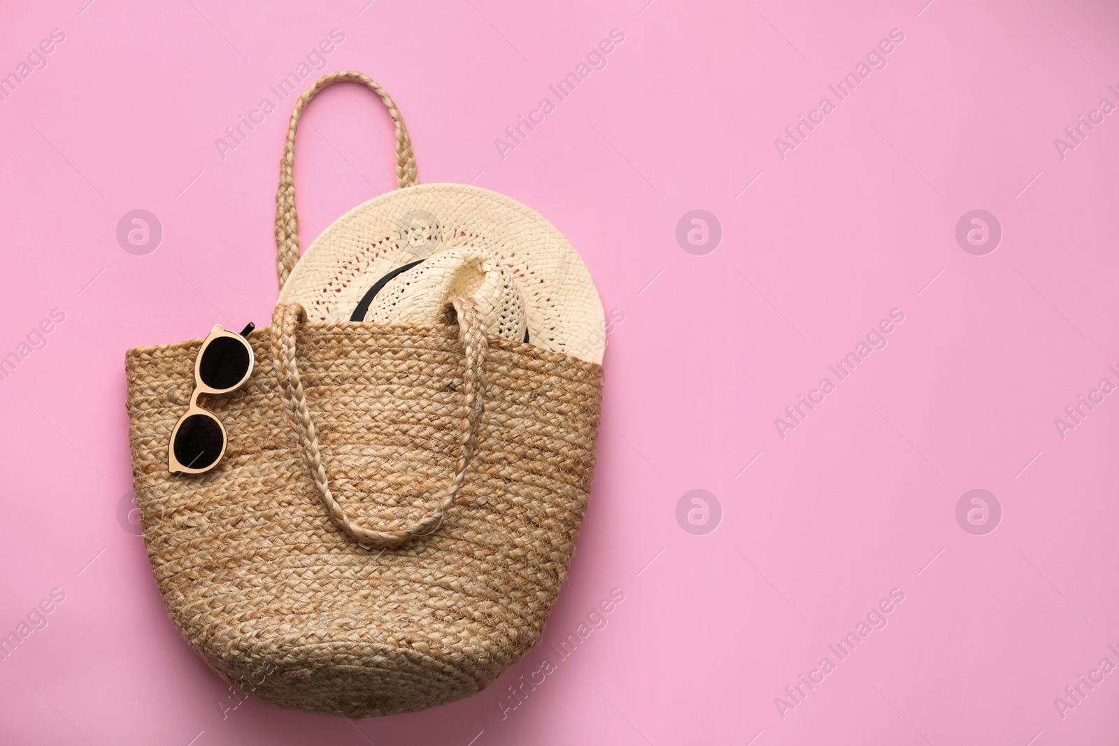 Photo of Elegant woman's straw bag with hat and sunglasses on pink background, top view. Space for text