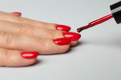 Photo of Woman painting nails with red polish on white background, closeup
