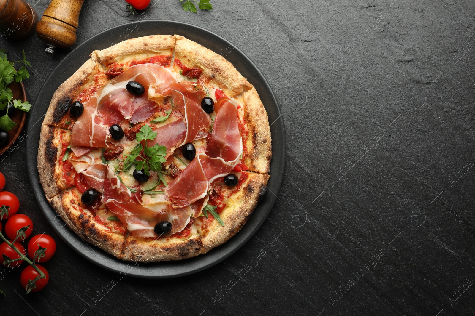 Photo of Tasty pizza with cured ham, olives, tomatoes and parsley on black table, top view. Space for text