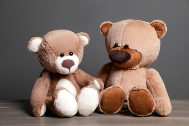 Photo of Cute teddy bears on wooden table near black wall