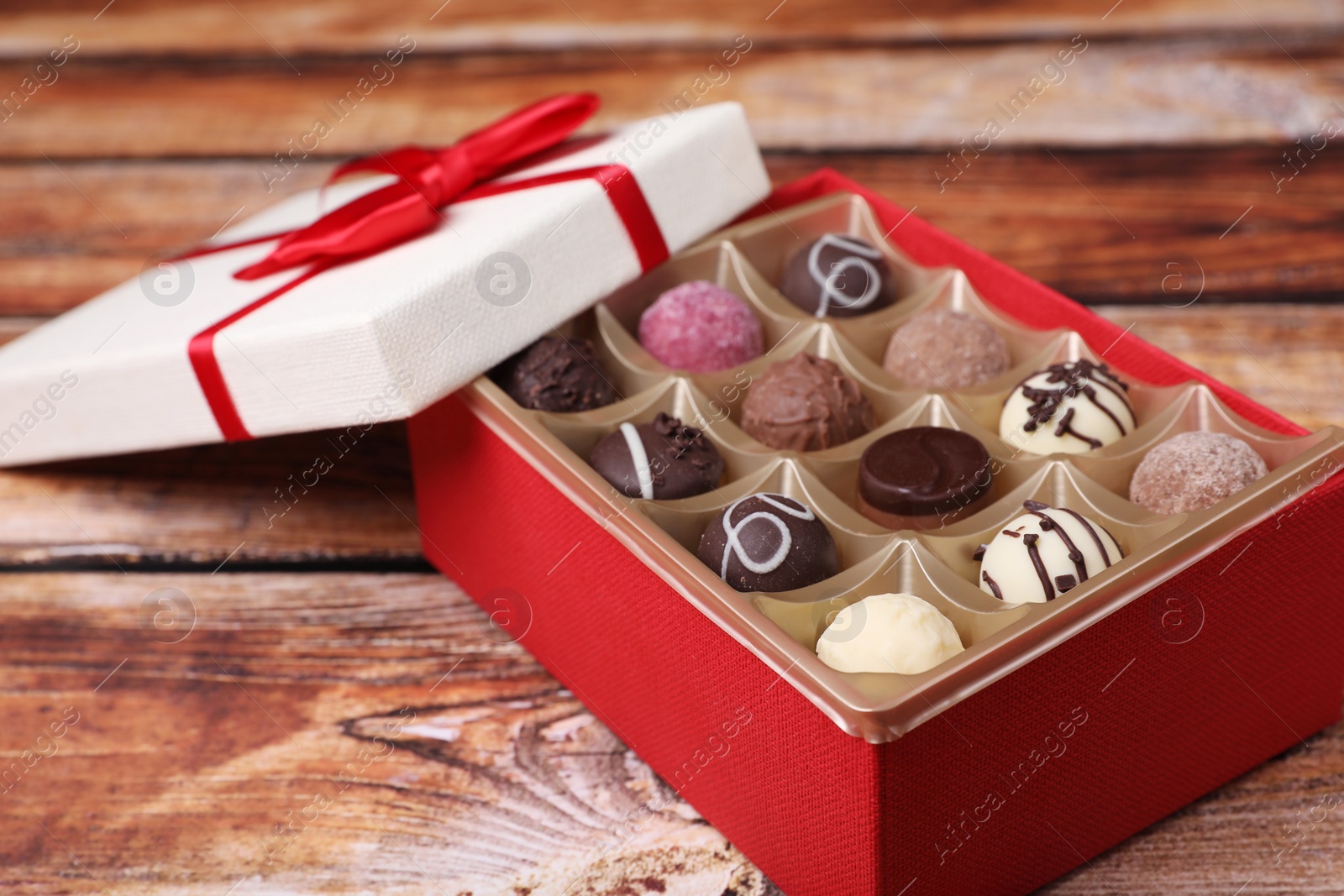 Photo of Red box with tasty chocolate candies on wooden table, closeup