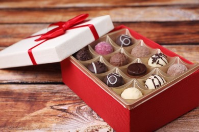 Photo of Red box with tasty chocolate candies on wooden table, closeup