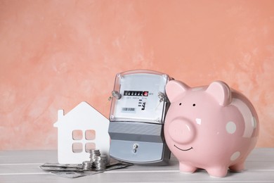 Photo of Electricity meter, piggy bank, house model and money on white wooden table