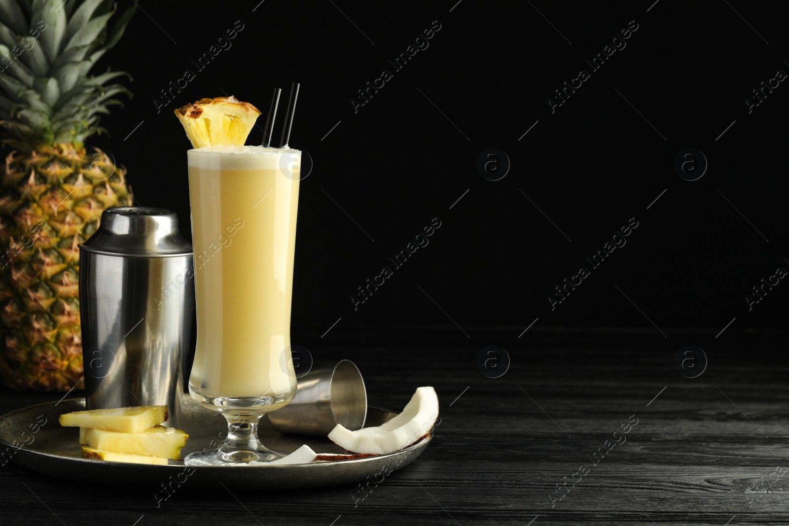 Photo of Tasty Pina Colada cocktail and ingredients on black wooden table, space for text