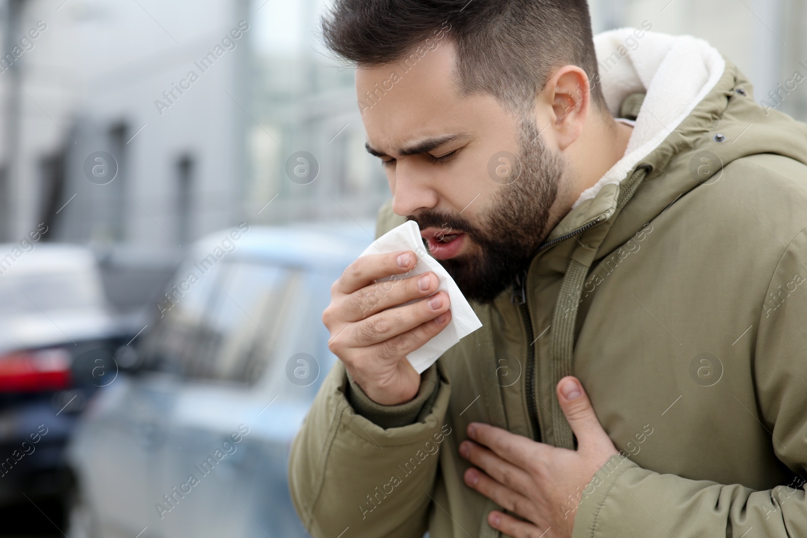 Photo of Sick man with tissue coughing outdoors. Cold symptoms