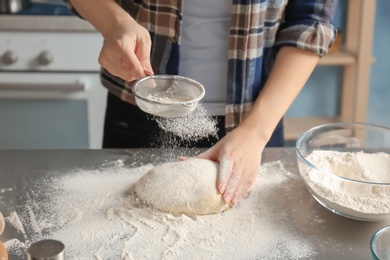 Photo of Woman sprinkling flour over dough on table in kitchen