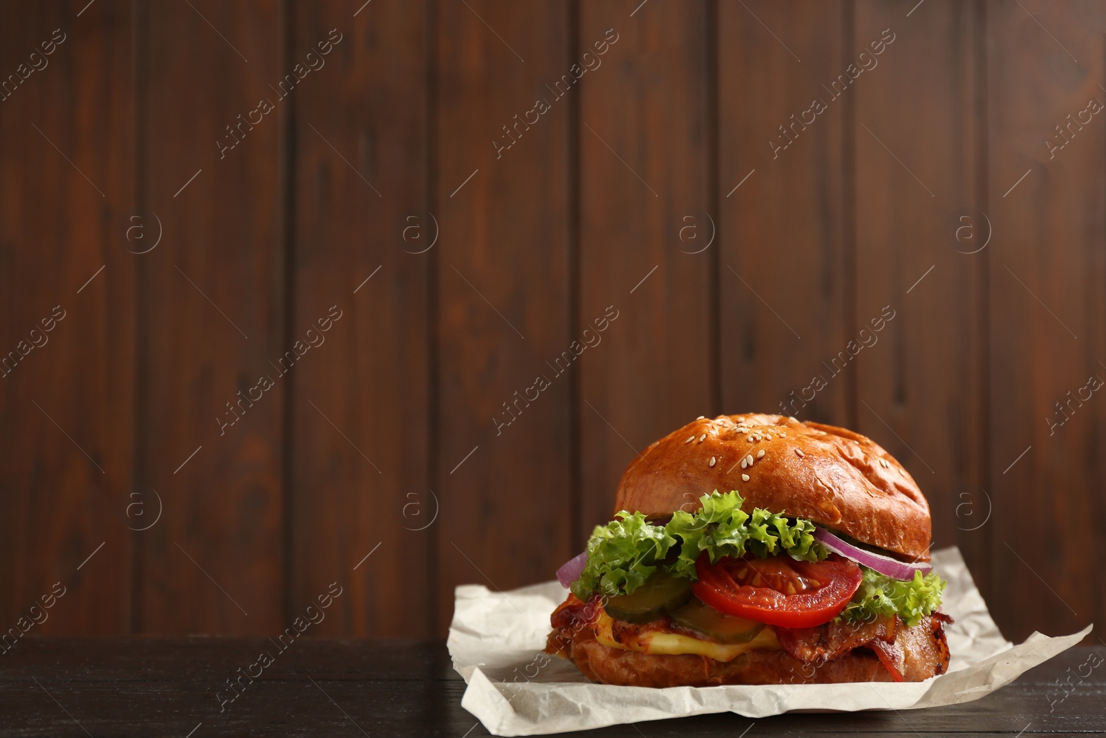 Photo of Delicious burger with bacon on table against blurred background. Space for text