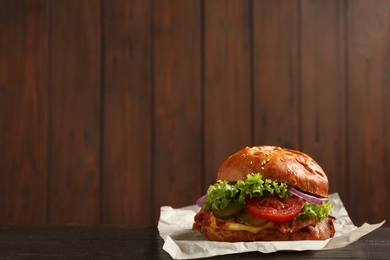 Photo of Delicious burger with bacon on table against blurred background. Space for text