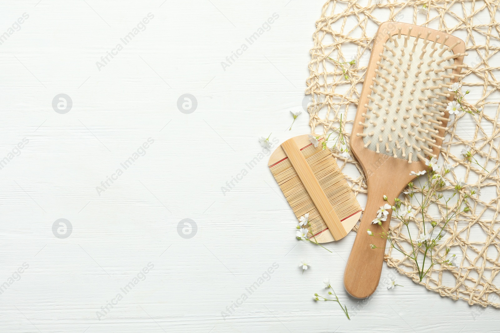 Photo of Hair brush, comb and small flowers on white wooden background, flat lay. Space for text