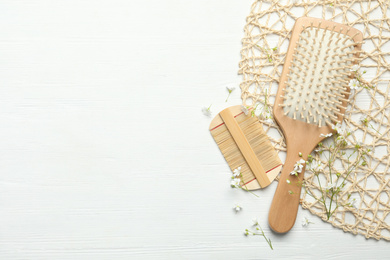 Hair brush, comb and small flowers on white wooden background, flat lay. Space for text