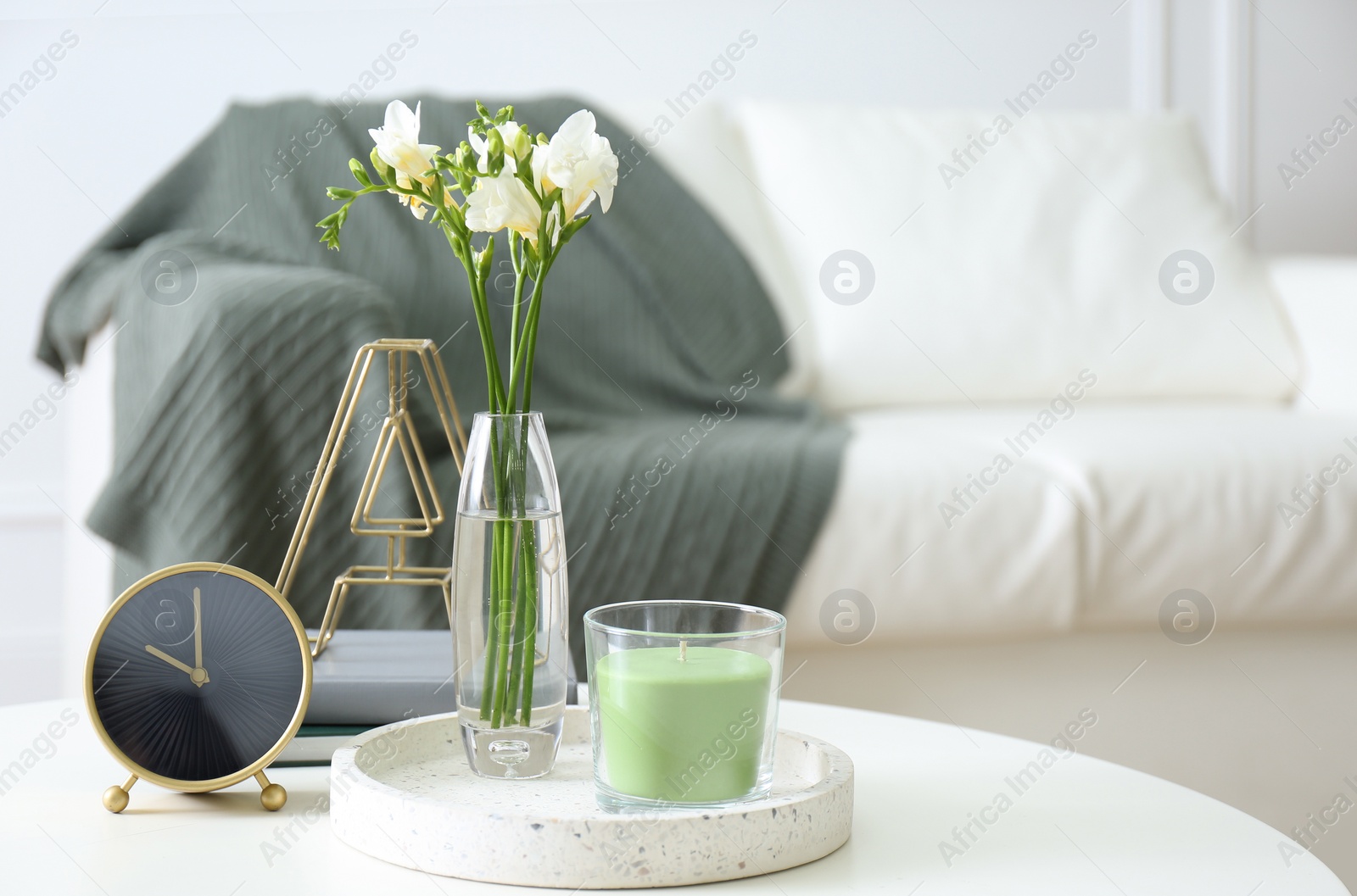 Photo of Vase with beautiful freesia flowers, candle and clock on table indoors, space for text. Interior elements