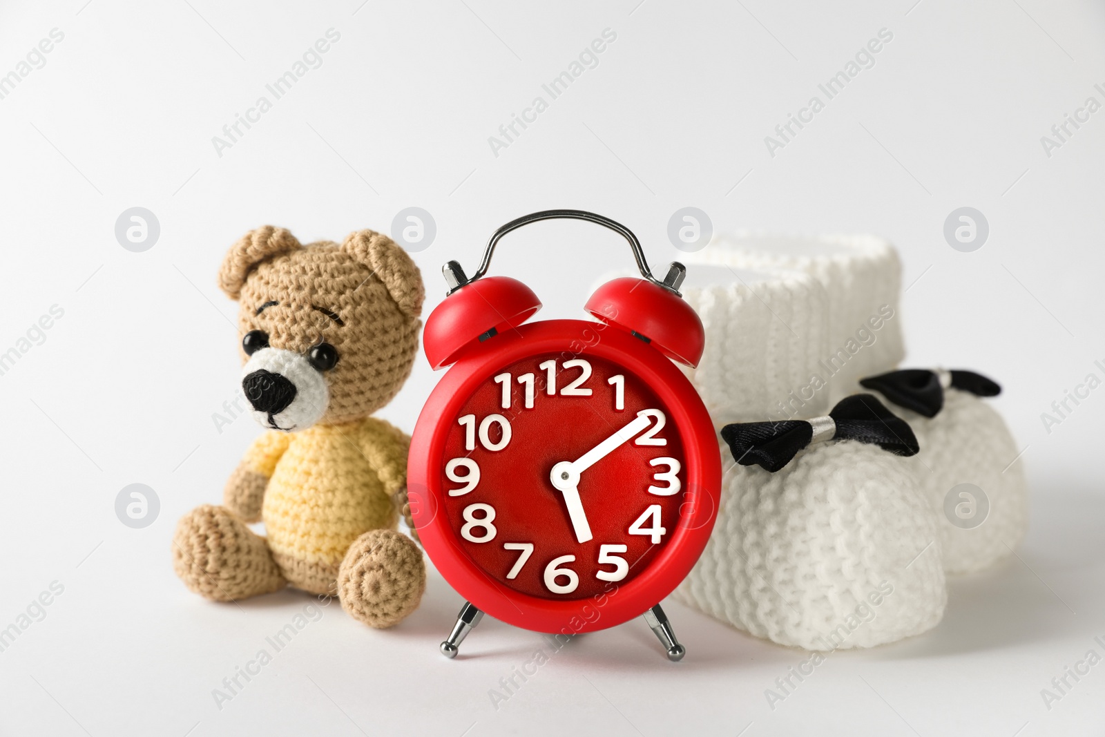 Photo of Alarm clock, toy bear and baby booties on white background. Time to give birth