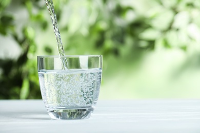 Photo of Pouring water into glass on white wooden table outdoors, space for text. Refreshing drink