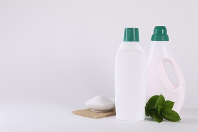 Bottles of cleaning product, baking soda and green leaves on white background