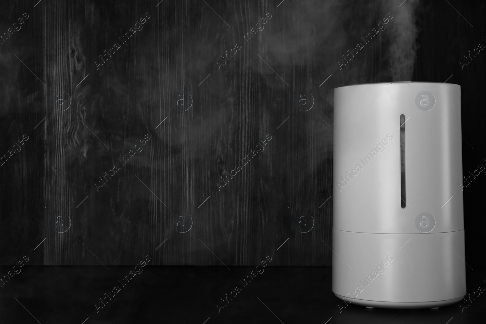 Photo of Modern air humidifier on table against wooden background. Space for text