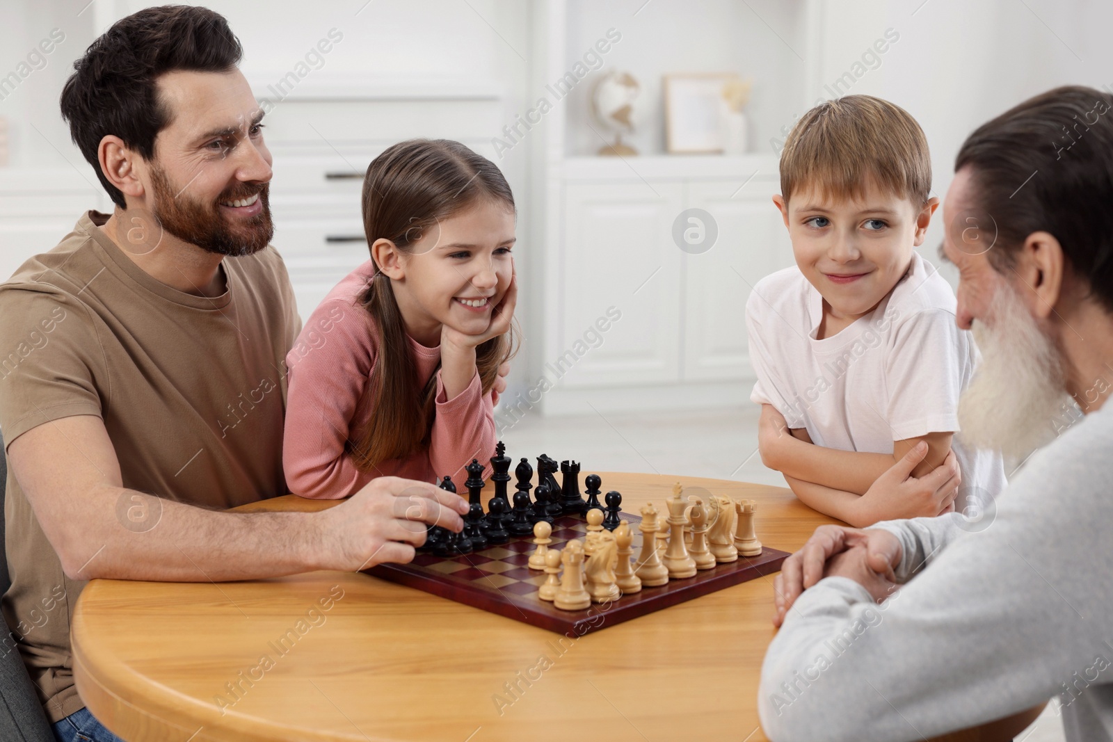 Photo of Family playing chess together at table in room