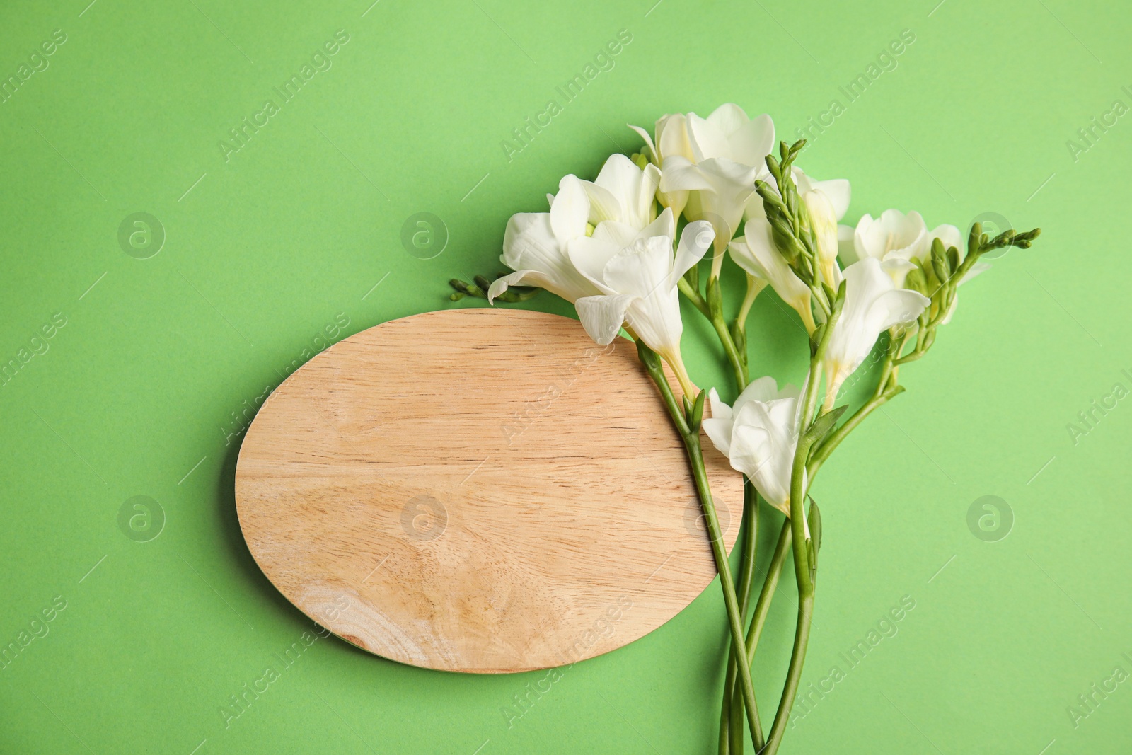 Photo of Beautiful spring freesia flowers and wooden board on green background, flat lay. Space for text