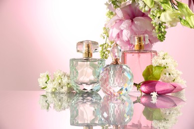 Photo of Luxury perfumes and floral decor on mirror surface against pink background. Space for text