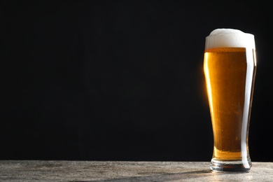 Photo of Cold tasty beer on grey table against dark background. Space for text