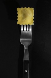 Photo of Fork with tasty ravioli on black table, closeup