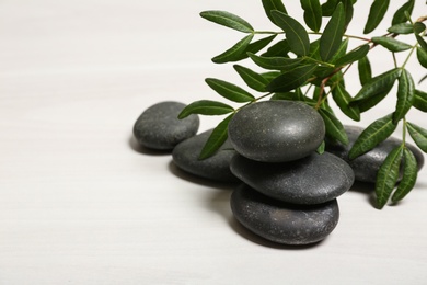 Photo of Spa stones and green leaves on white table, space for text