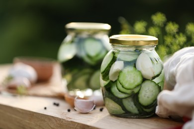 Jar of delicious pickled cucumbers and ingredients on wooden table against blurred background, closeup. Space for text
