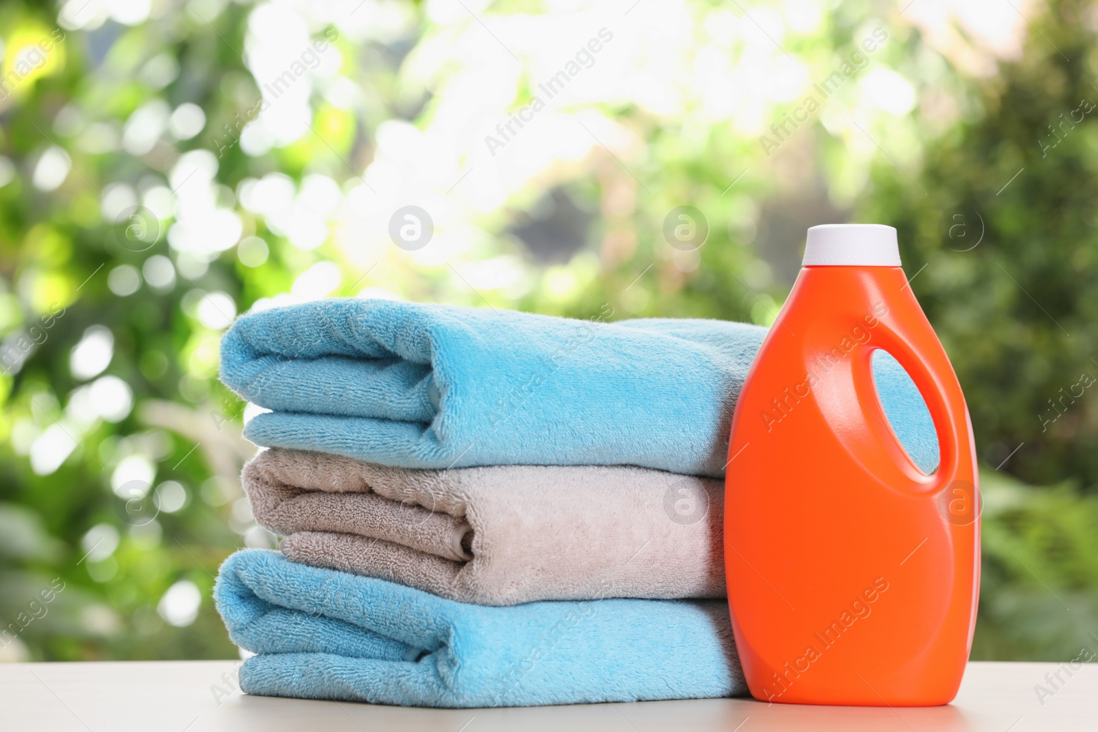 Photo of Soft bath towels and laundry detergent on table against blurred background