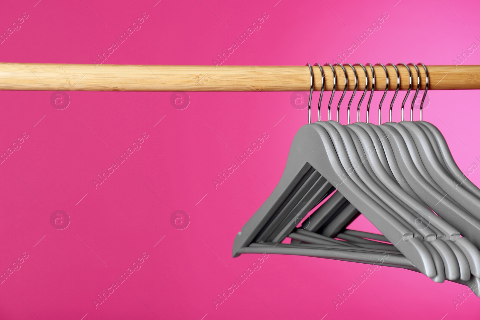 Photo of Wooden rack with clothes hangers on color background, space for text