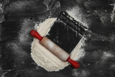 Flour and rolling pin on black table, top view. Space for text