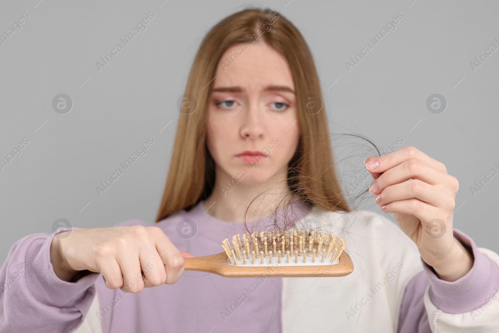 Photo of Woman untangling her lost hair from brush on light grey background, selective focus. Alopecia problem