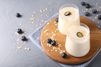 Photo of Tasty yogurt in glasses, oats and blueberries on grey table, space for text