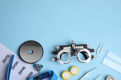 Different ophthalmologist tools on light blue background, flat lay. Space for text