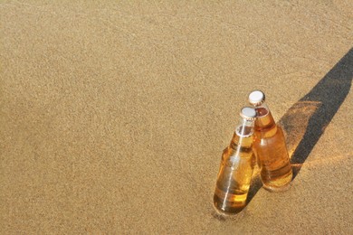 Photo of Bottles of cold beer on sandy beach, space for text