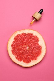 Photo of Pipette with citrus essential oil and fresh grapefruit slice on pink background, flat lay