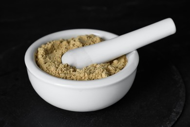 Photo of Mortar with mustard powder on black table, closeup