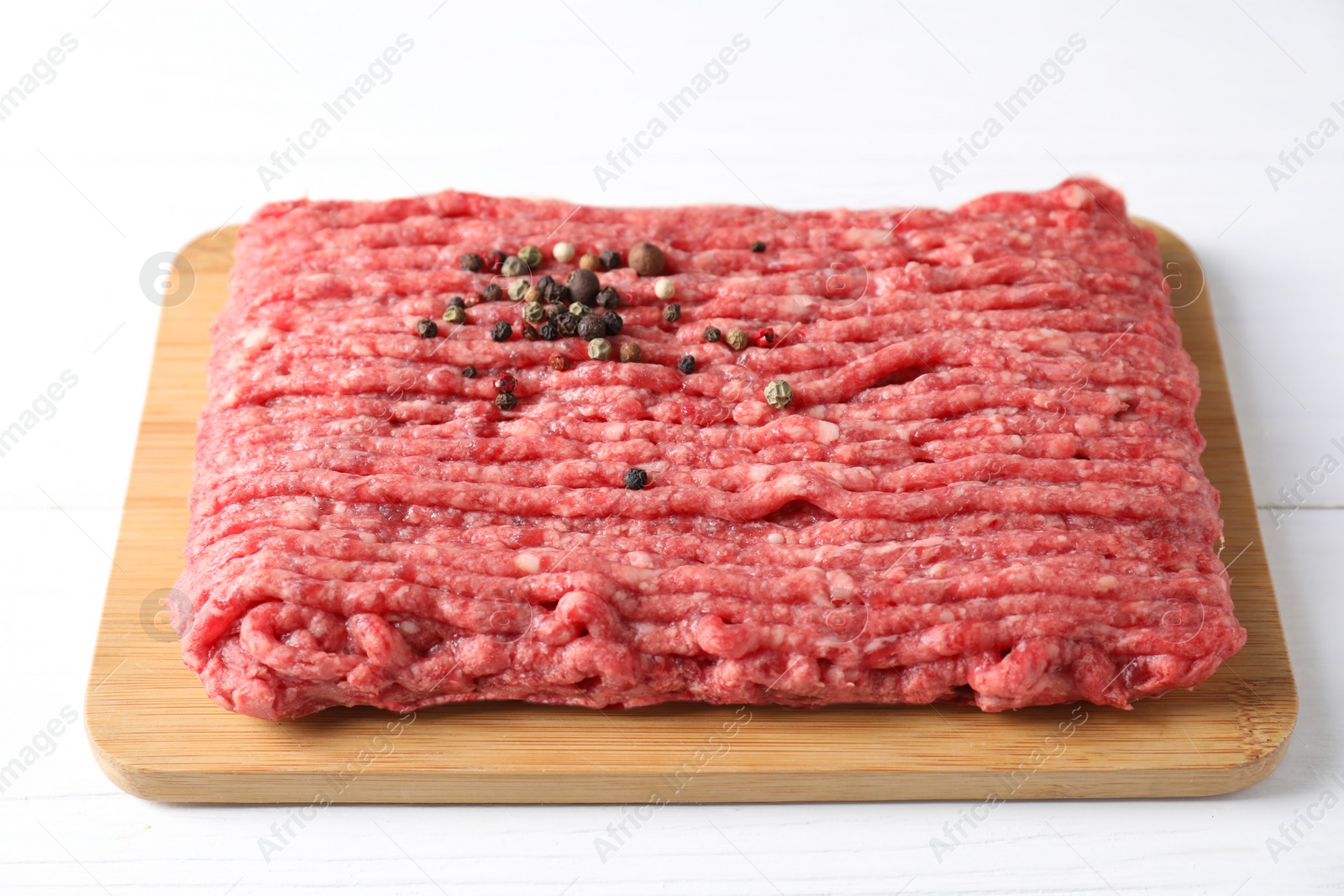 Photo of Raw ground meat and peppercorns on white wooden table