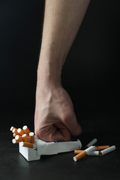 Photo of Stop smoking. Man crushing pack with cigarettes on dark background, closeup