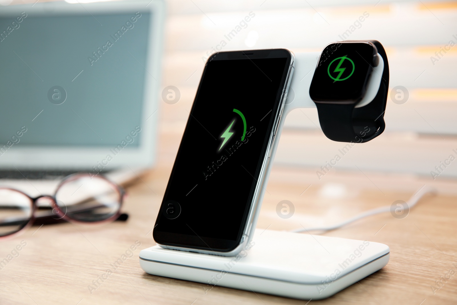 Photo of Mobile phone and smartwatch with wireless charger on wooden table. Modern workplace accessory