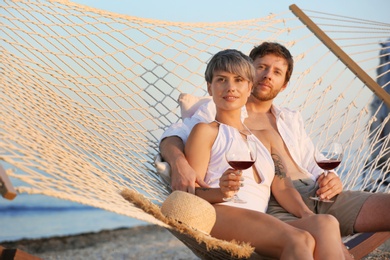 Young couple resting with glasses of wine in hammock on beach