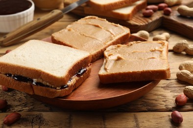 Photo of Tasty peanut butter sandwiches with jam and peanuts on wooden table, closeup