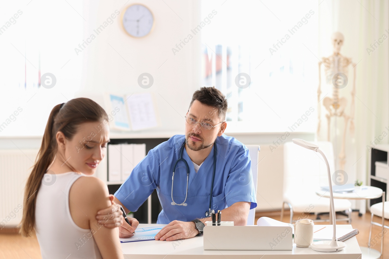 Photo of Male orthopedist examining patient with injured arm in clinic