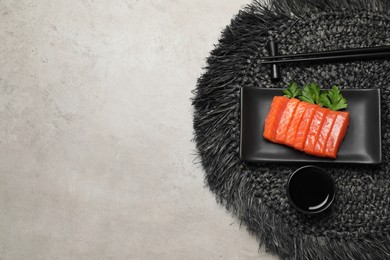 Plate of tasty salmon slices, soy sauce and parsley on grey table, top view with space for text. Delicious sashimi dish