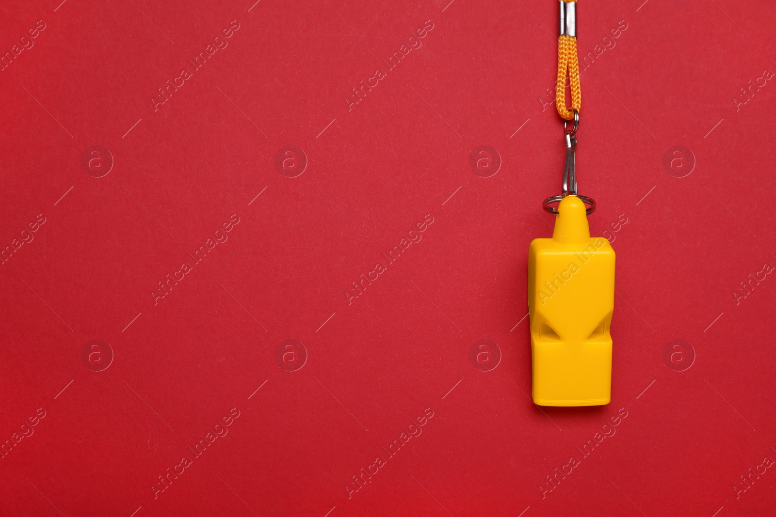 Photo of One yellow whistle with cord on red background, top view. Space for text