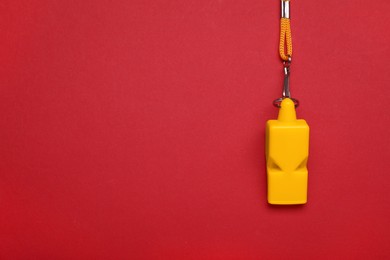 Photo of One yellow whistle with cord on red background, top view. Space for text