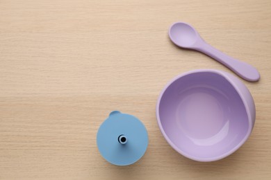 Photo of Set of plastic dishware on wooden background, flat lay with space for text. Serving baby food