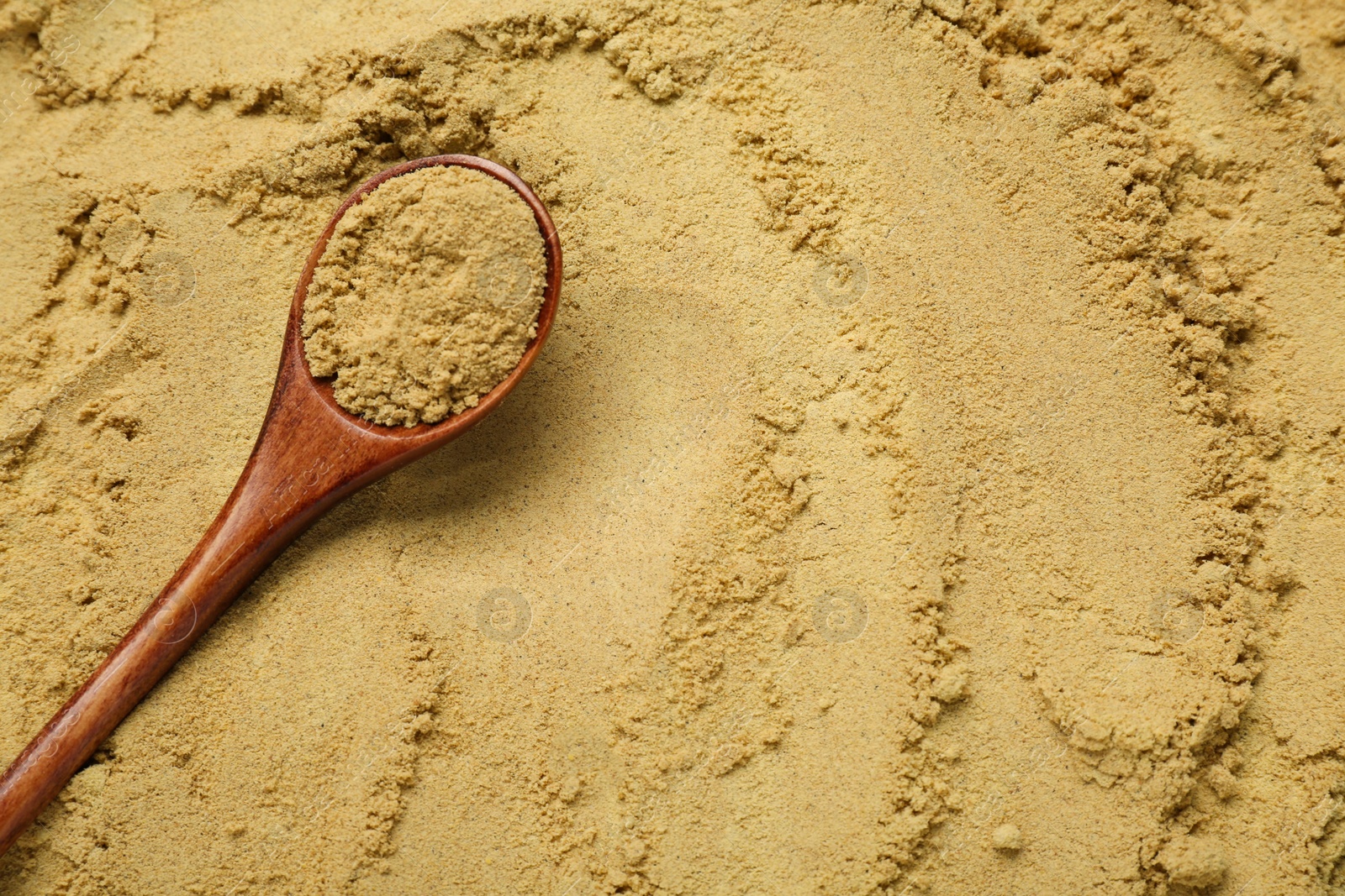 Photo of Heap of aromatic mustard powder and wooden spoon, top view. Space for text