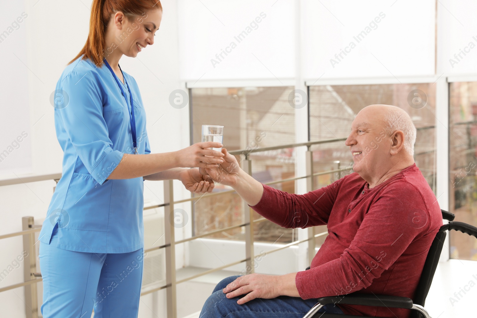 Photo of Nurse giving water to senior man in wheelchair at hospital. Medical assisting